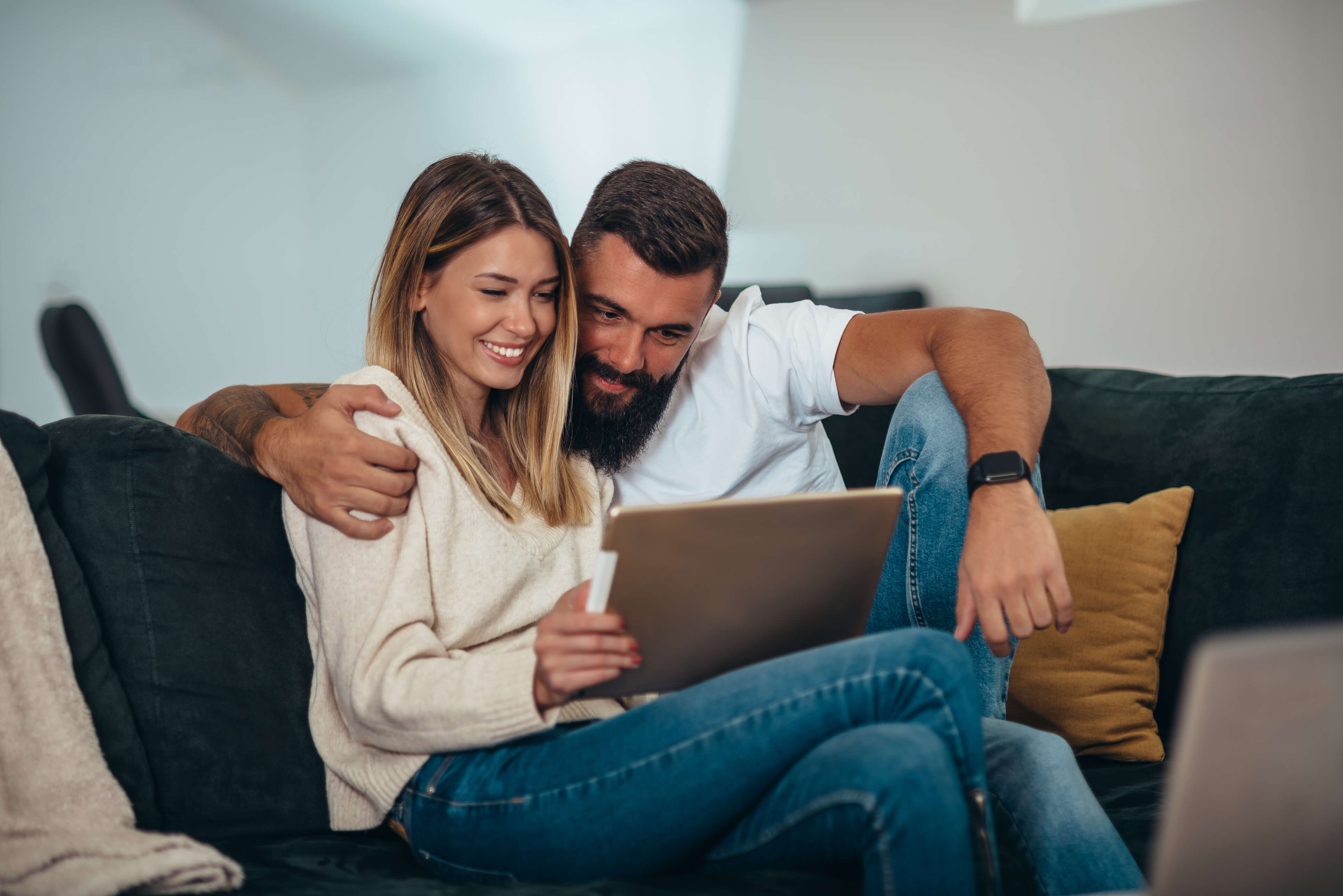 Pareja joven sonriendo sentada en un sofá mirando una laptop.